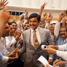 a man in a suit and tie stands in a crowd of people