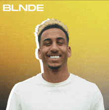 a man in a white shirt is smiling in front of a yellow background that says blnde