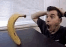 a man is sitting at a table with his mouth open while a banana is sitting on the table .