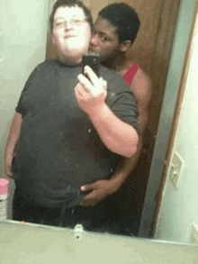 a man is taking a selfie with another man in front of a mirror .