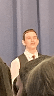 a young man in a suit and tie stands in front of a blue curtain .