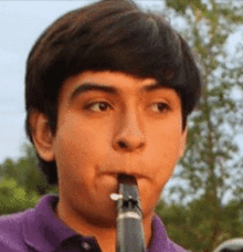 a young man in a purple shirt is playing a clarinet outside