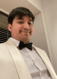 a man in a white tuxedo and black bow tie smiles