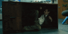a man in a suit and tie is crawling under a wooden desk