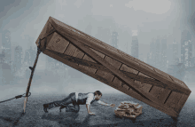 a man crawling under a large wooden box with a city in the background