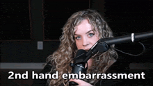 a woman in front of a microphone with the words " 2nd hand embarrassment " written below her