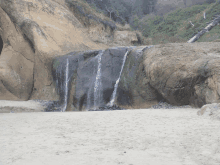 a waterfall is surrounded by rocks and trees on a sandy beach