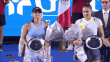 two female tennis players holding trophies and flowers in front of a banner that says ' mexico ' on it