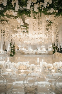 a large room filled with tables , chairs , flowers , and chandeliers .