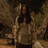 a woman wearing a fur coat and a knitted top stands in the dirt