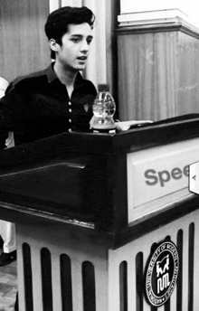 a young man stands behind a podium that says spec