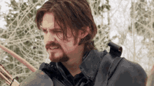 a man with long hair and a beard is holding an arrow