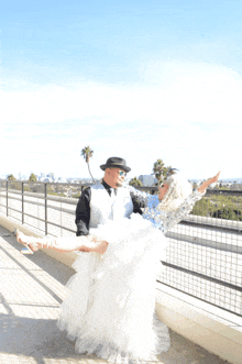 a man in a hat is holding a woman in a white dress in his arms