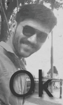 a black and white photo of a man wearing sunglasses with the word ok behind him