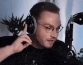 a man wearing headphones and glasses is talking into a microphone while sitting in front of a microphone .