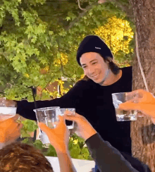 a man wearing a black beanie is toasting with glasses