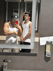 two men are taking a selfie in a bathroom mirror with a sign on the wall that says please make sure all doors are closed