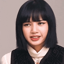 a close up of a woman with short black hair and bangs wearing a white shirt and a black vest .