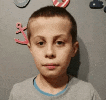 a young boy in a gray shirt is standing in front of a wall with anchors on it .