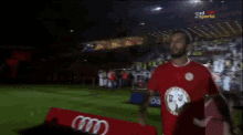 a man in a red shirt stands on a soccer field in front of a sign that says ' coca cola '