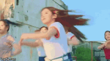 a group of young girls are dancing in front of a building while their hair blows in the wind .