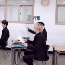 a group of people are sitting at desks in a classroom with a clock on the wall above them .