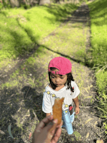 a little girl wearing a pink hat and a white t-shirt with circles on it is being held by someone