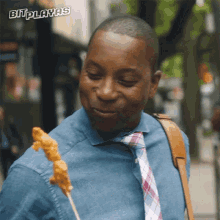 a man in a denim shirt and tie is eating a skewer of food with the words bitplayas above him