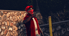 a man wearing a bandana and a red hat is standing in front of a stone wall