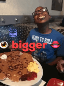 a boy wearing a blue shirt that says ready to roll is sitting at a table with a plate of food in front of him