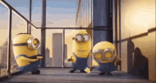 a group of minions are standing on a balcony in front of a window .