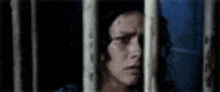 a man is behind bars in a jail cell and looking out of the bars .