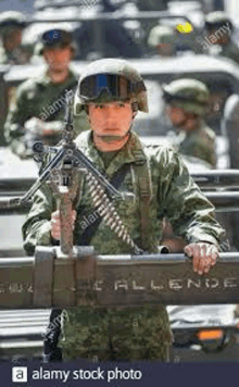 a mexican soldier is holding a machine gun in front of a military vehicle .