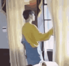 a man in a yellow sweater is standing next to a window in a room .