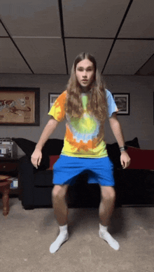 a man with long hair and a tie dye shirt is dancing in a living room