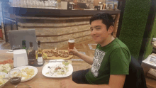 a boy wearing a green shirt that says ' nirvana ' on it holds a glass of beer