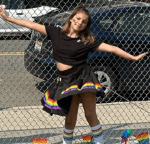 a young girl wearing a rainbow skirt and socks stands in front of a chain link fence