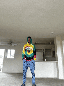 a man wearing a tie dye jamaica hoodie is standing in an empty room