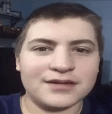 a close up of a young man 's face with a blue shirt on making a funny face .