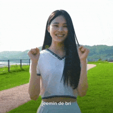 a girl in a white crop top is standing in a grassy field with the words jeemin de bri written above her