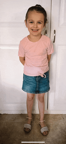 a little girl wearing a pink shirt and denim skirt