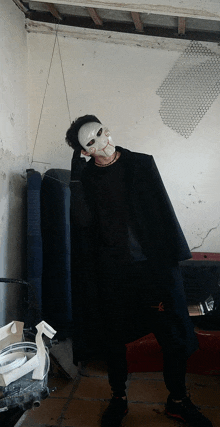 a man wearing a white mask and a black coat is standing in a room