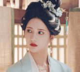 a close up of a woman 's face with a pearl necklace and a flower in her hair