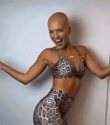 a bald woman in a leopard print top and leggings is smiling and dancing .