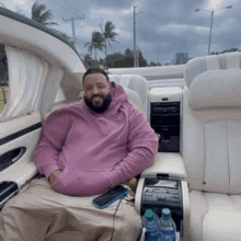 a man in a pink hoodie is sitting in the back seat of a car with bottles of water .