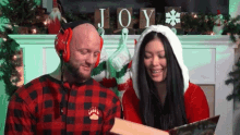 a man and a woman are reading a book in front of a fireplace with a sign that says joy on it