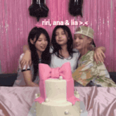 three girls are hugging in front of a pink cake with the words riri ana & lia above them