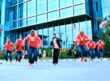 a group of people are jumping in the air in front of a building that has a reflection of the american flag