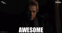 a man wearing a scarf and a jacket is standing in a dark room and says awesome .