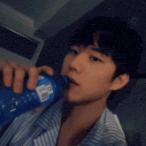 a young man is drinking from a blue bottle with a white label